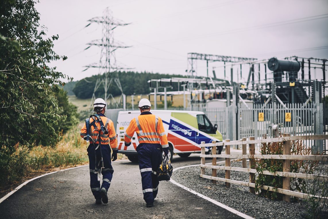 Two engineers wearing PPE and carrying equipment walking at substation