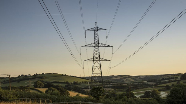 Electricity pylon with overhead lands in a hilly green landscape