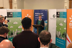 Rhian Kelly standing in front of business banner stands, addressing audience of men, women and photographers - used for the National Grid story 'All-party parliamentary group working together to deliver net zero'