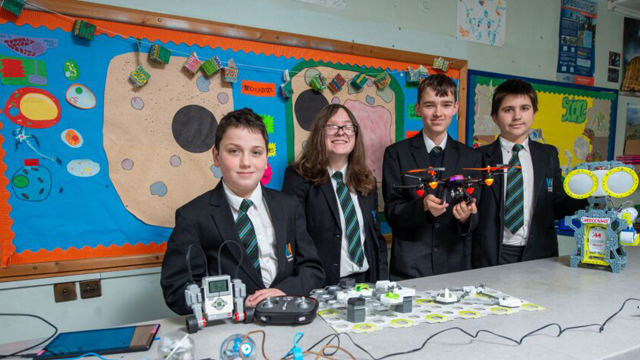 Young students wearing school uniform behind table with STEM equipment, including a drone