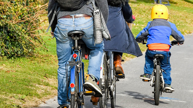 Two adults and a child wearing a yellow helmet cycling on path