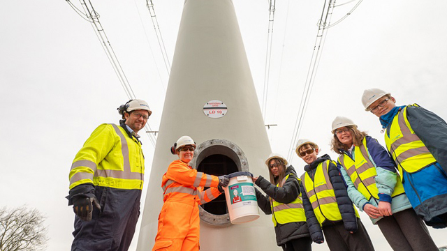 Students wearing hard hats and high-vis vests placing time capsule inside t-pylon