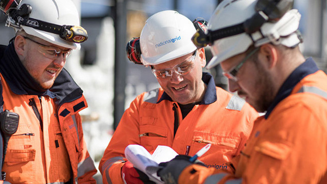 Three National Grid construction engineers wearing hard hats and PPE discussing paperwork