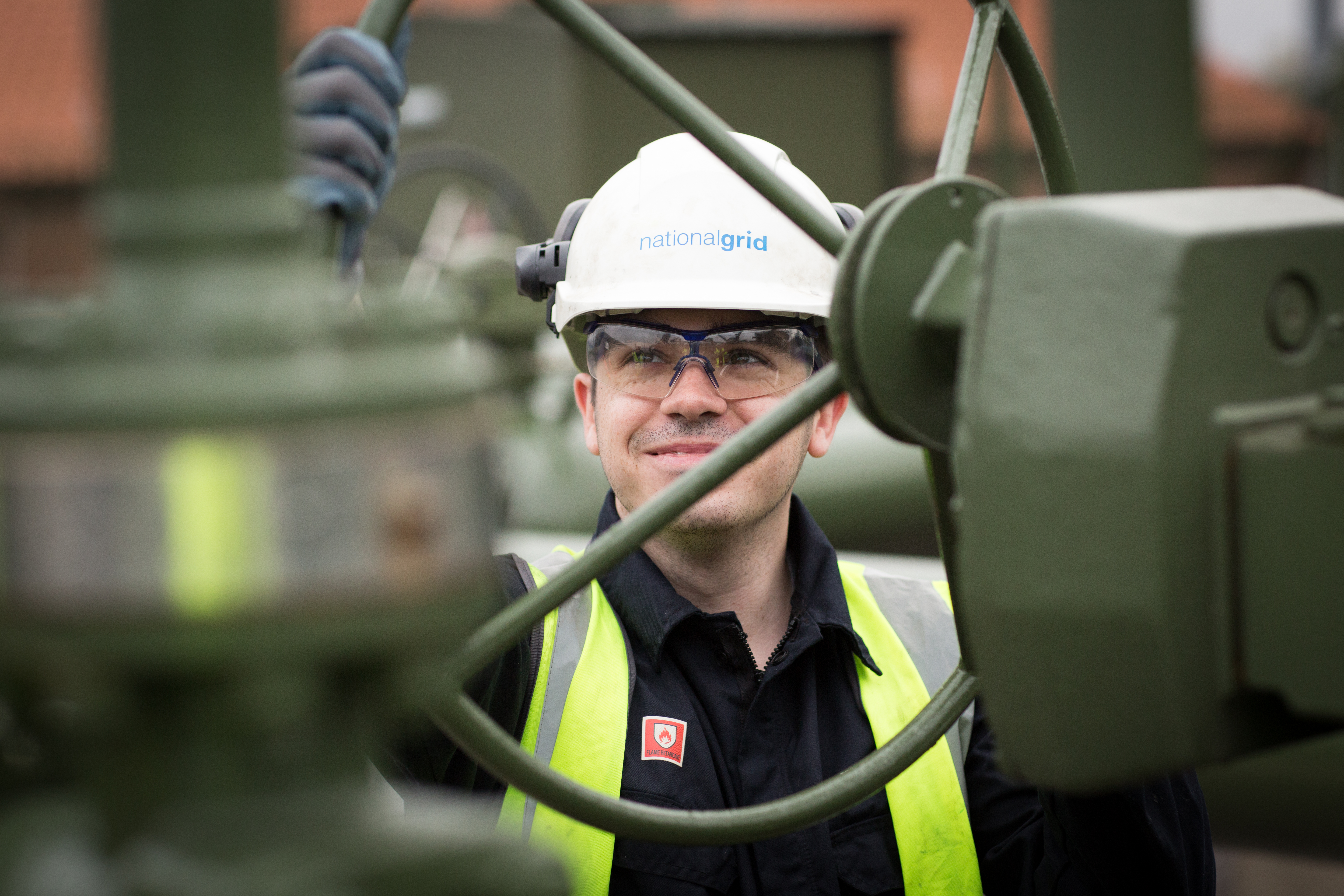 An image of a gas engineer working on-site, wearing a hard hat and a hi-vis vest
