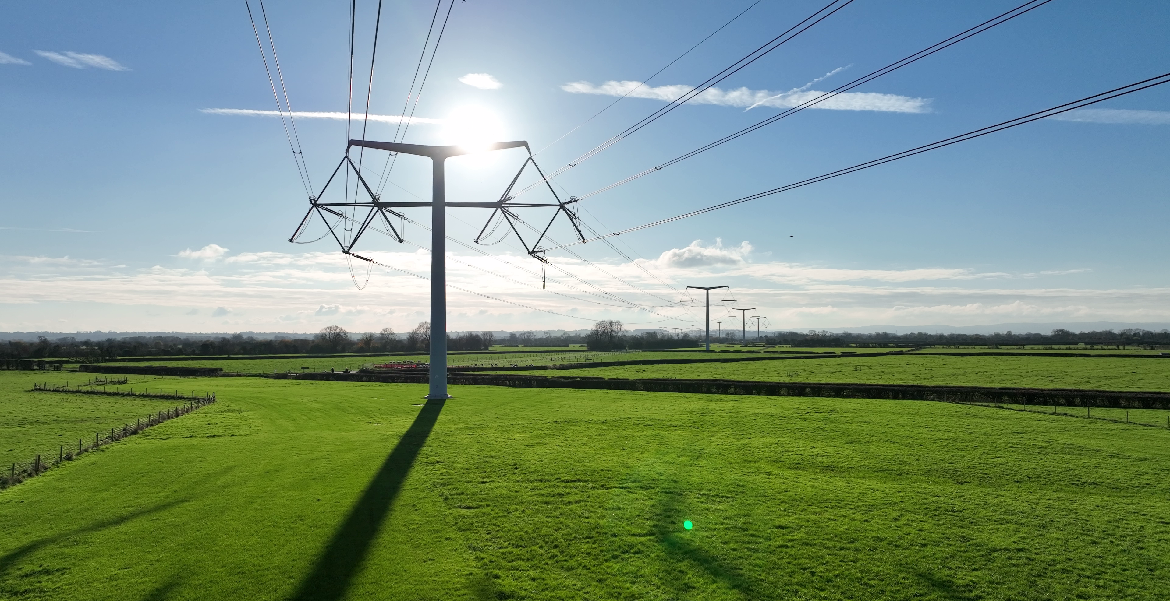 T-pylons and overhead electricity lines in the sunshine in green fields