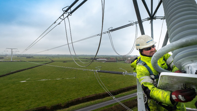 Man wearing PPE at height working on stringing new T-pylon overhead lines