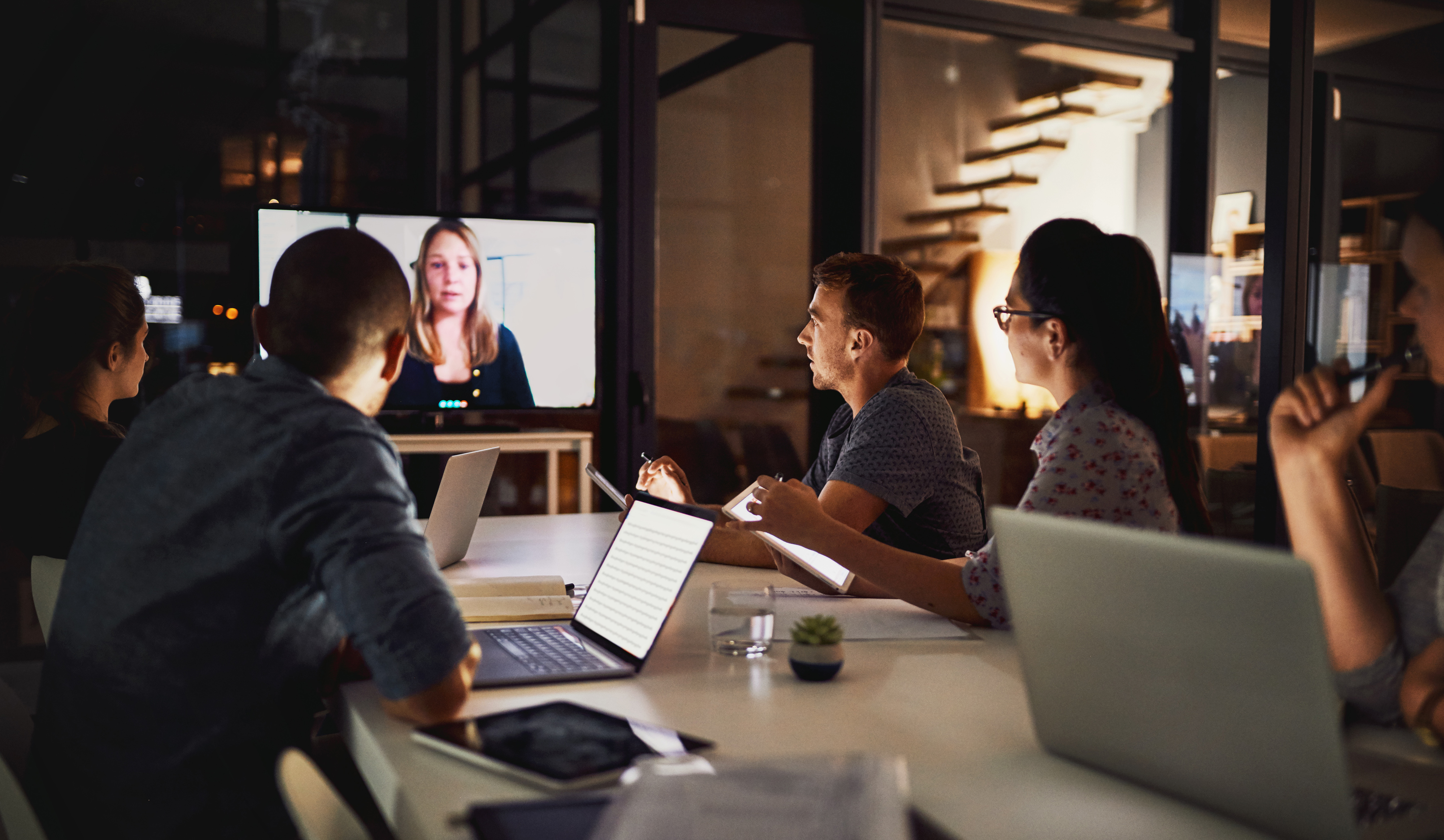 People sitting around conference table with one lady on a video screen