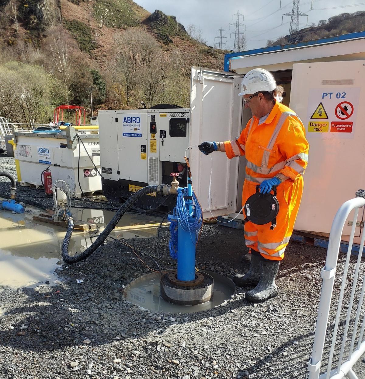 Worker in high-visibility PPE undertaking a pump test on site in Eryri