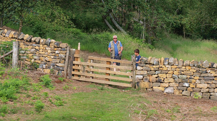 Man and boy coming towards wooden gate in a dry-stone wall