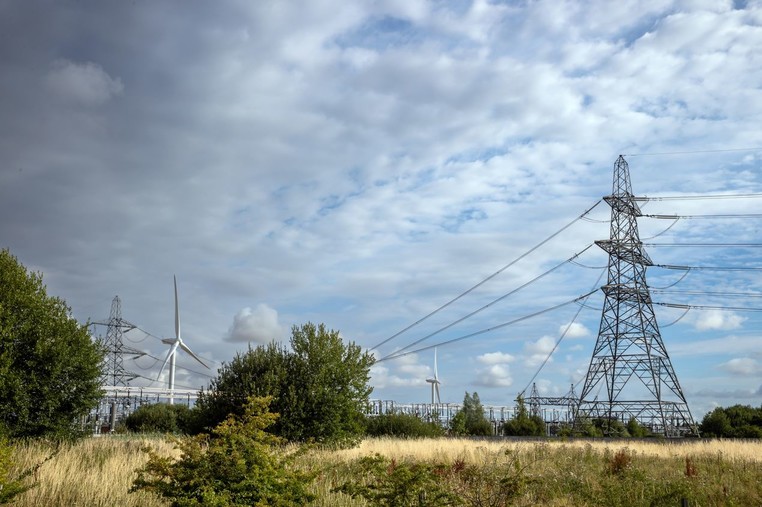 Pylons and electricity transmission lines by an electricity substation with wind turbines in the background