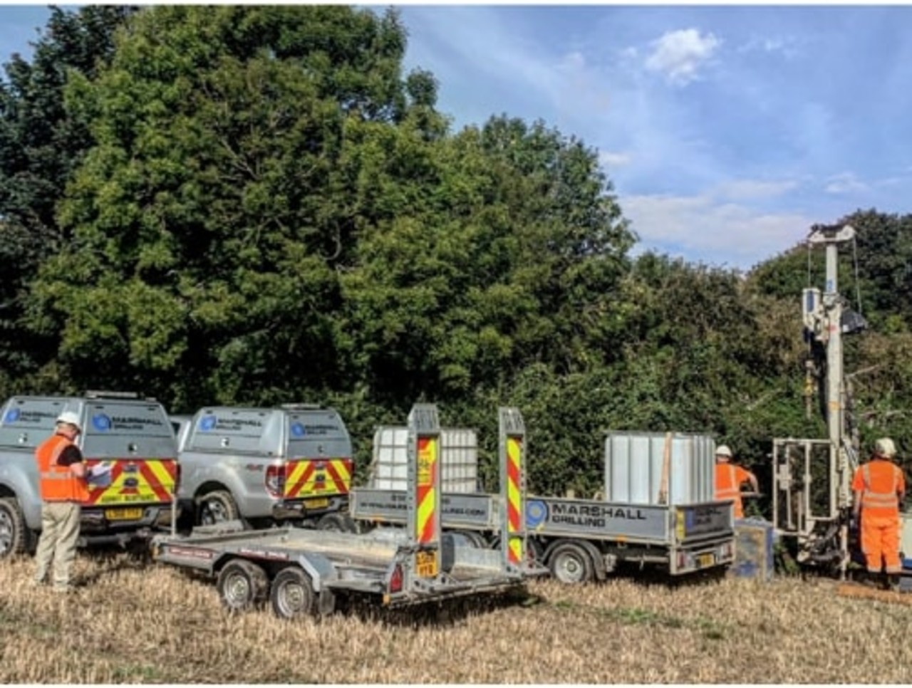 Contractors wearing orange high-vis PPE working in a field next to cars with trailers