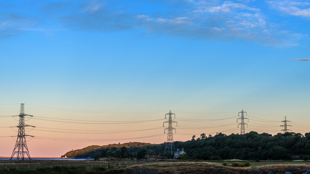 Transmission electricity pylons and overhead lines over estuary in Wales at sunrise