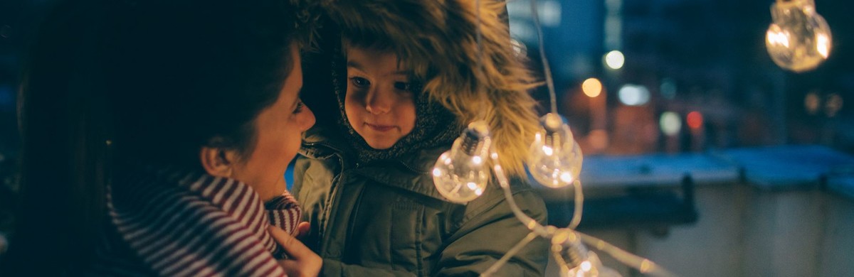 Mother and child wearing winter clothing among a string of solar-powered light bulbs
