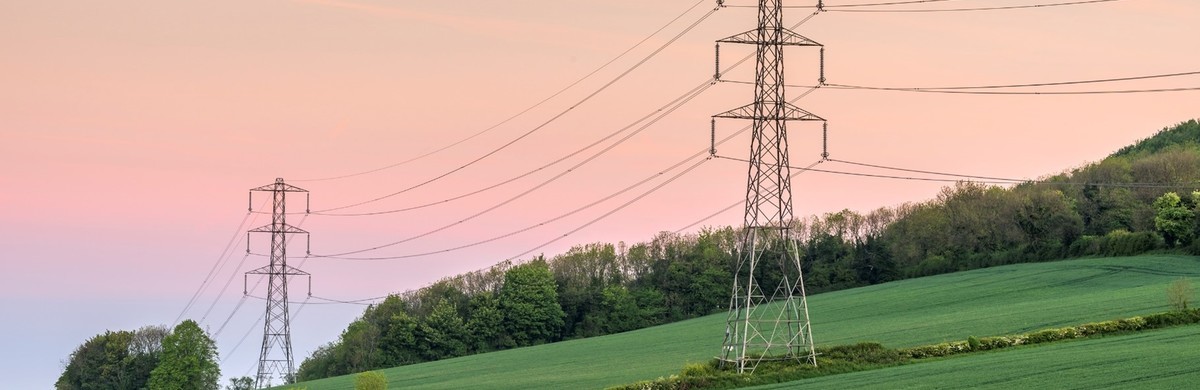 Transmission electricity lines and pylons set against a pink sunset