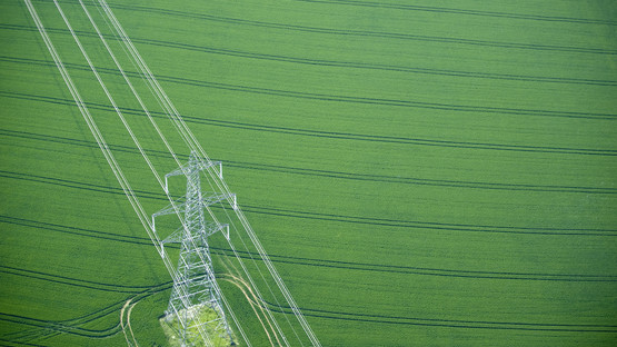 Electricity transmission pylon and overhead lines running across fertile green field