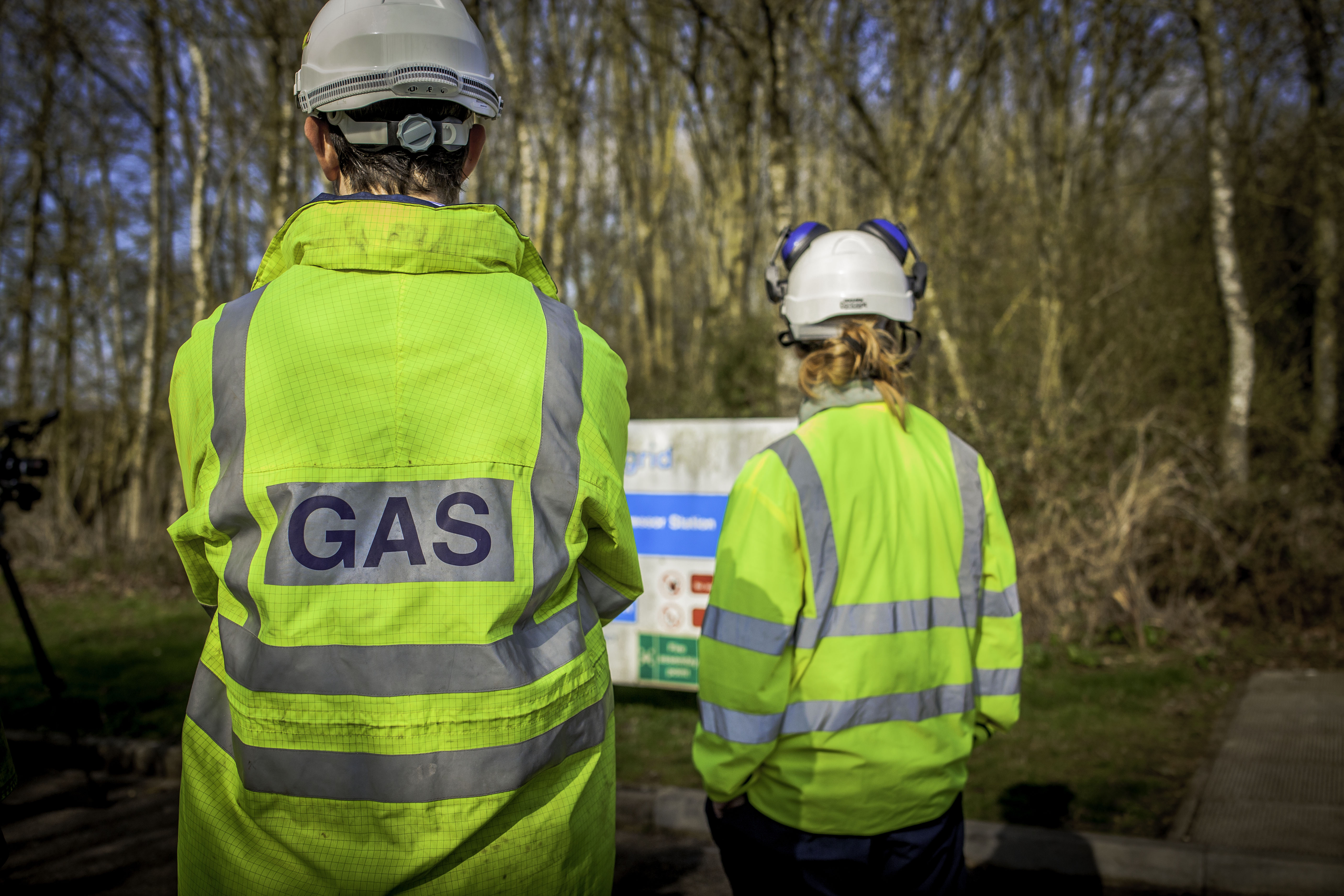 Two engineers wearing high visibility jackets in front of a wooded compressor site
