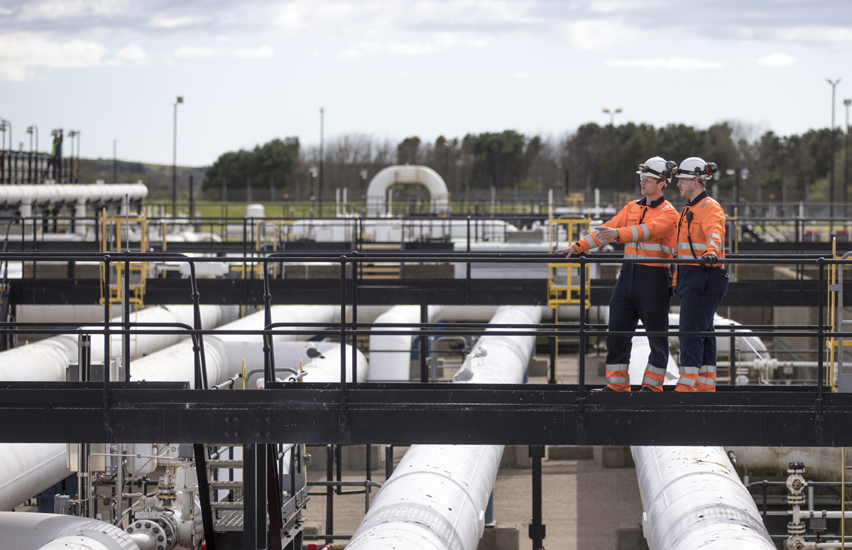 Two engineers with hard hats and high-vis overalls inspecting the gas terminal at StFergus, Scotland
