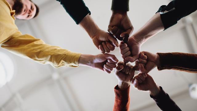 People standing in a circle holding their fists in seen from underneath