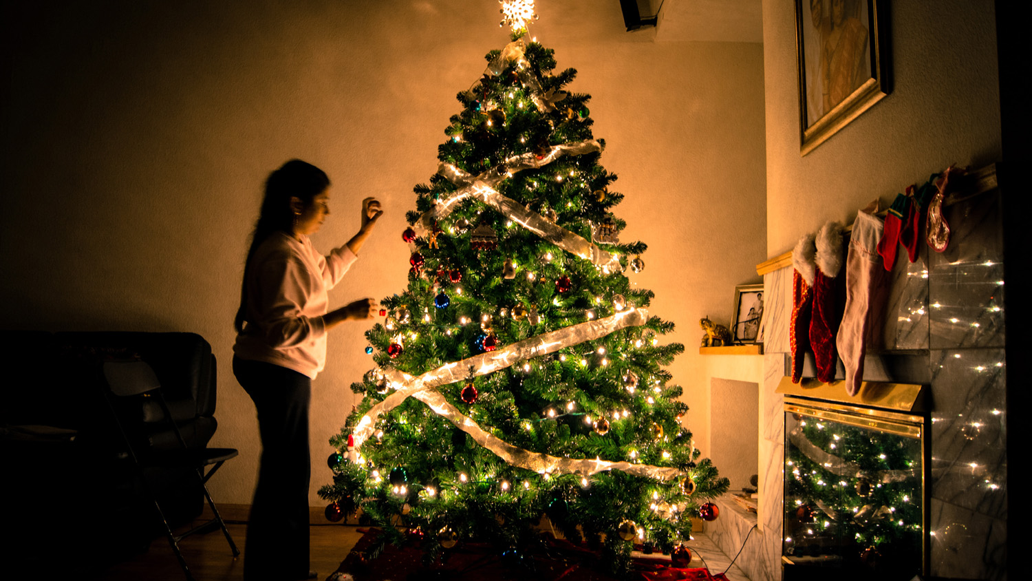 Girl decorating a lit Christmas tree in a semi-lit festively decorated room - used for the National Grid story 'The Christmas 'energy effect' revealed'