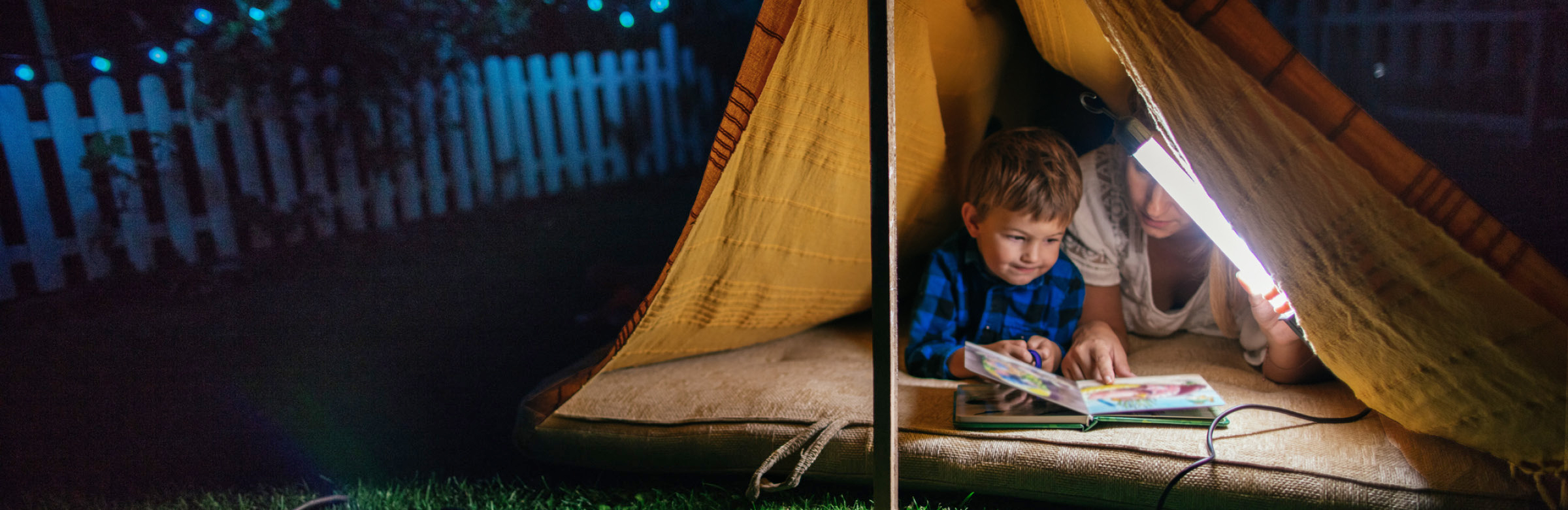 A woman and child reading in a tent with a garden scene in the background