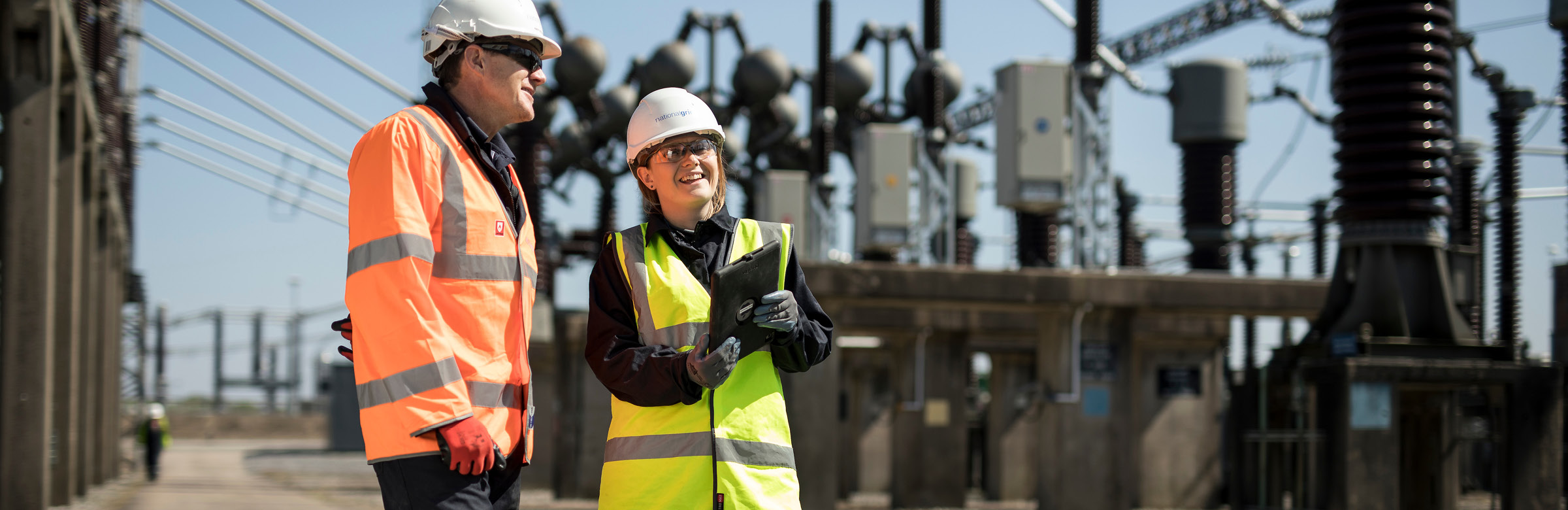 Two National Grid employees talking in front of an industrial framework
