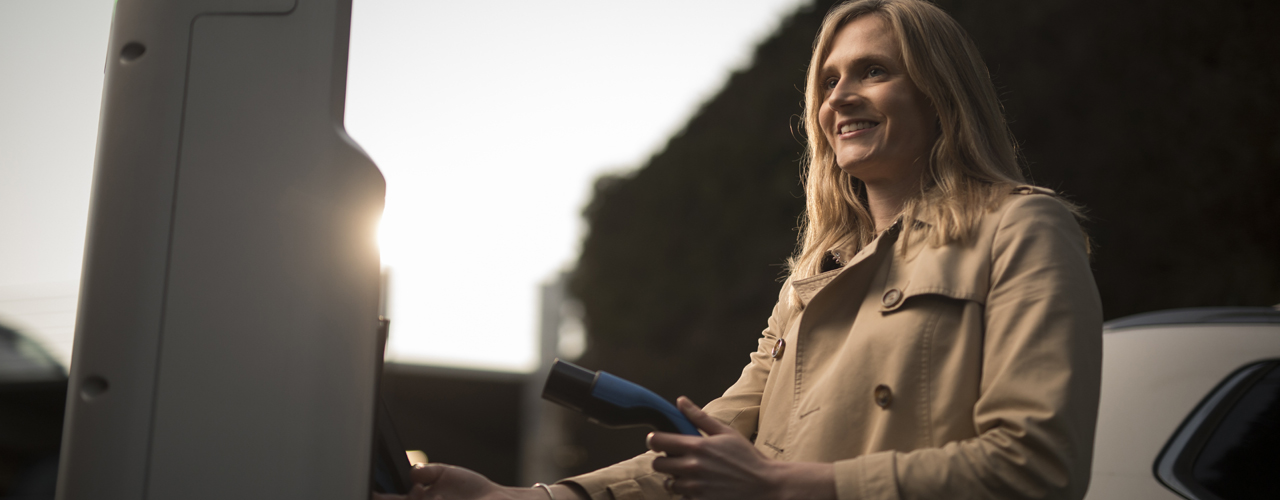 Woman wearing a trench coat about to put an EV charger into a charging point