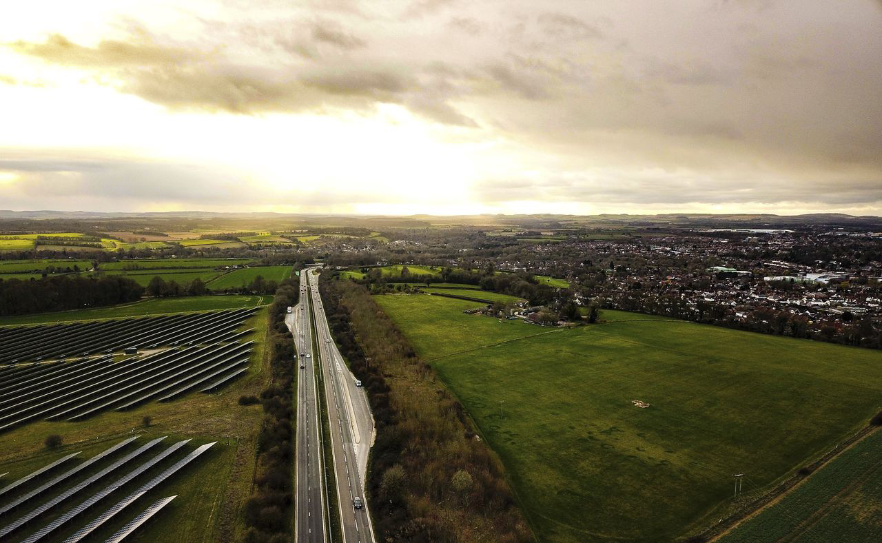 Road running between green fields with solar panels on the left