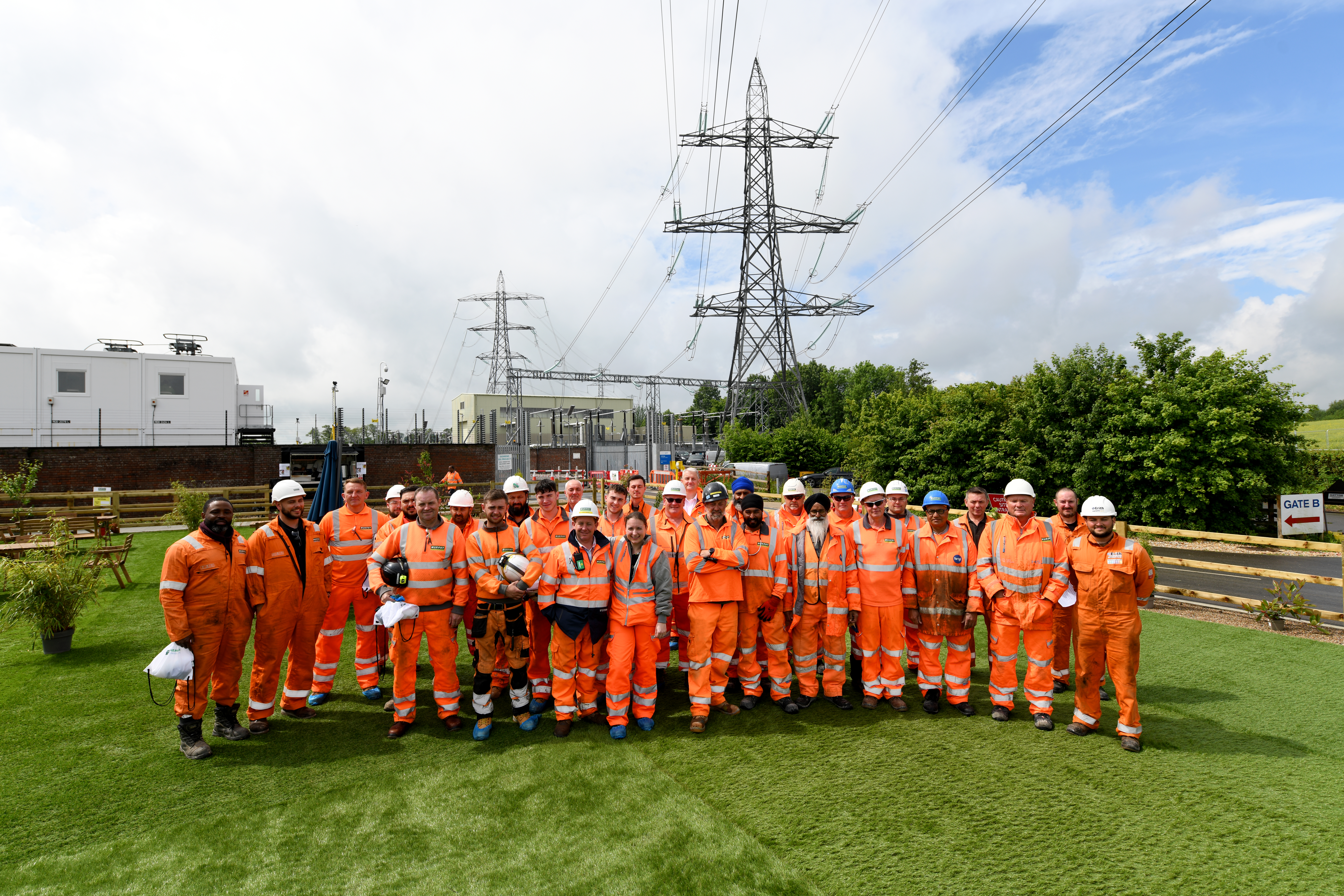 National Grid's construction health hub team wearing orange overalls in a green field with pylons in the background