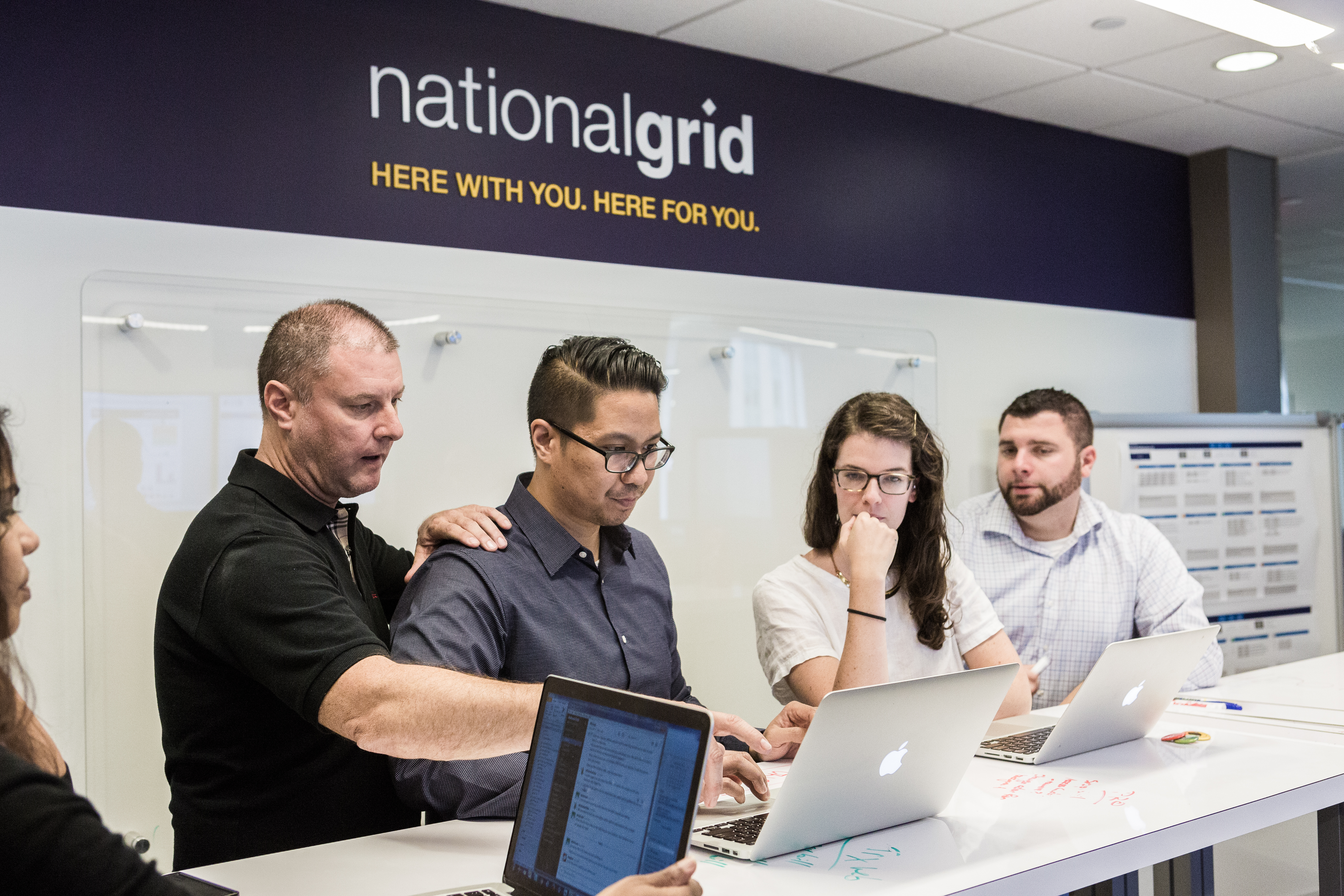 Five National Grid representatives working at a high desk with a white board in the background 