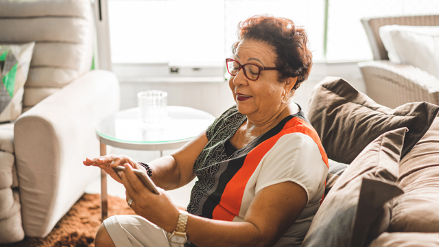 Lady on sofa looking at a mobile phone - National Grid's Grid for Good conference calls for elderly in Syracuse