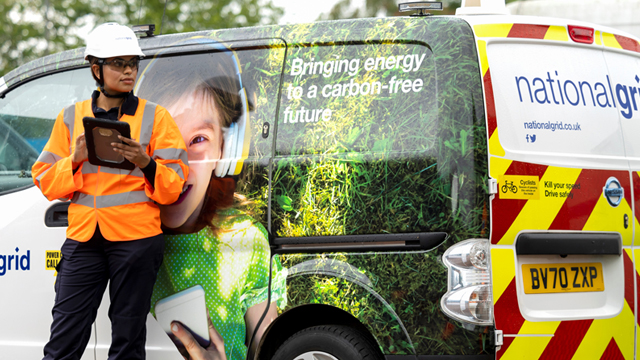 Engineer wearing PPE and holding smart device leaning against a National Grid Electricity Distribution van