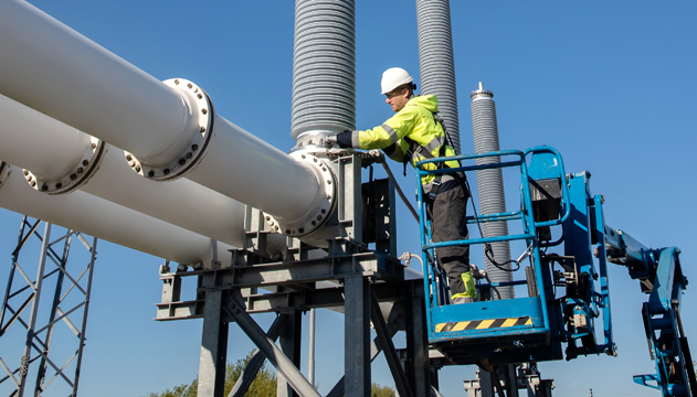 Engineer wearing PPE working from a cherry-picker on electricity switchgear at a substation