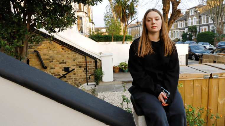 Young woman with long hair sitting on the banister of a house in an urban street