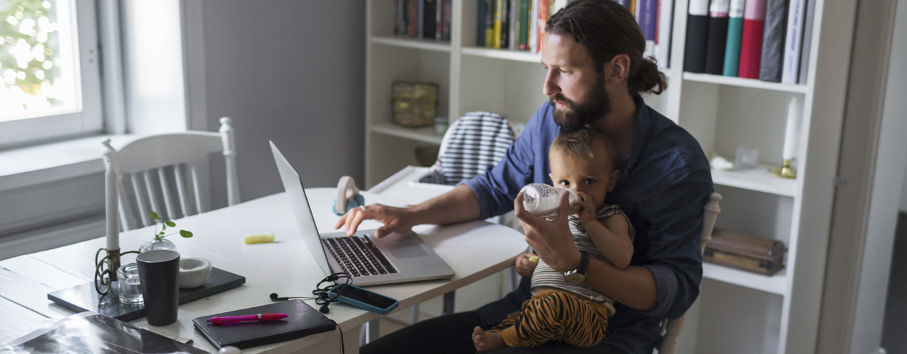 Man working on laptop holding a baby - used for the National Grid story 'Mental health comes first - especially in a crisis'