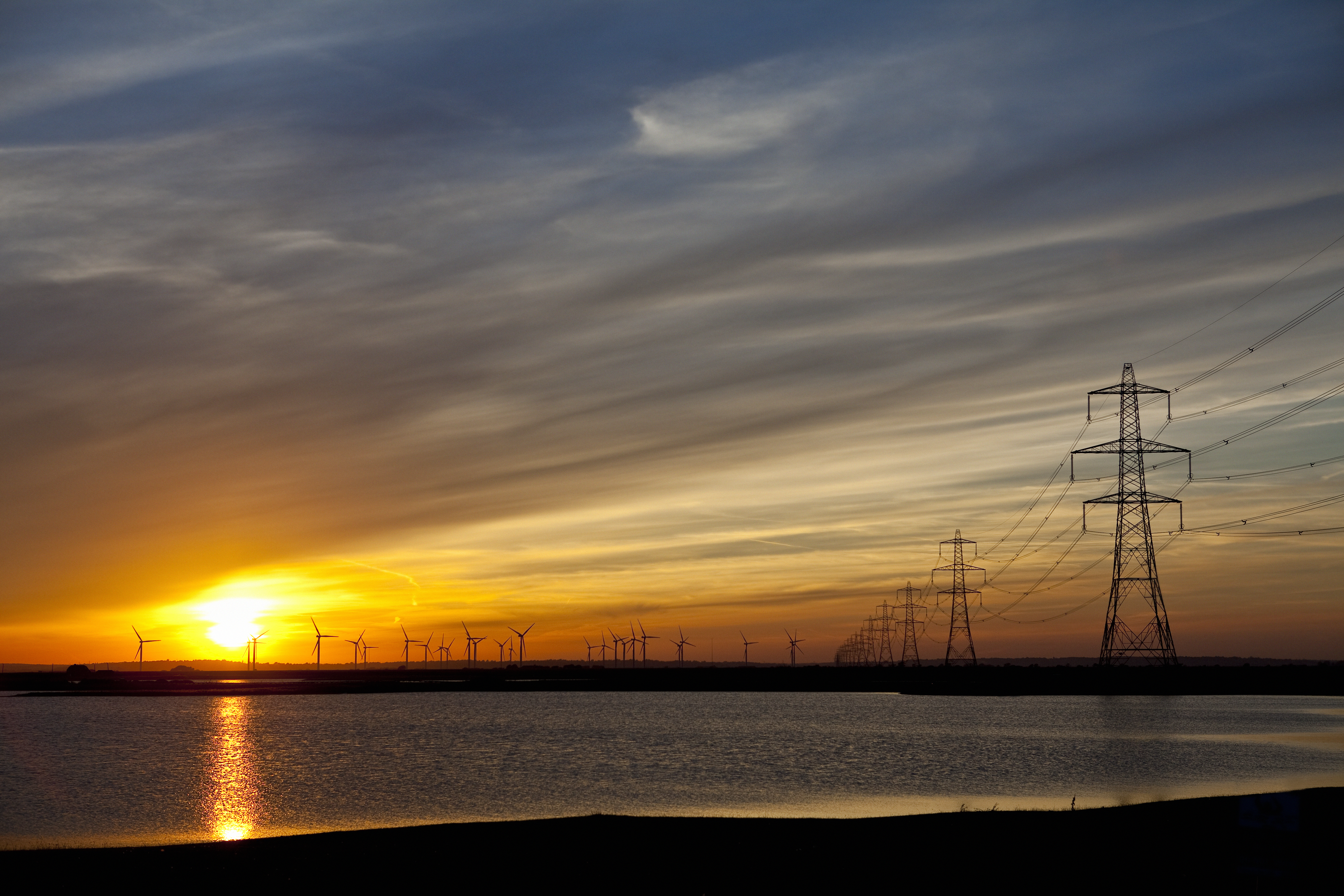 A beach at sunset with the sea coming in and electricity pylons dotted into the distance
