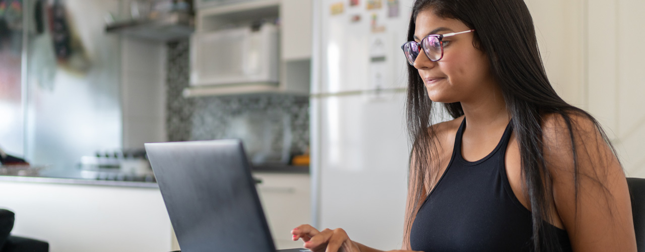 Young woman at kitchen table working on laptop for National Grid virtual interview skills story