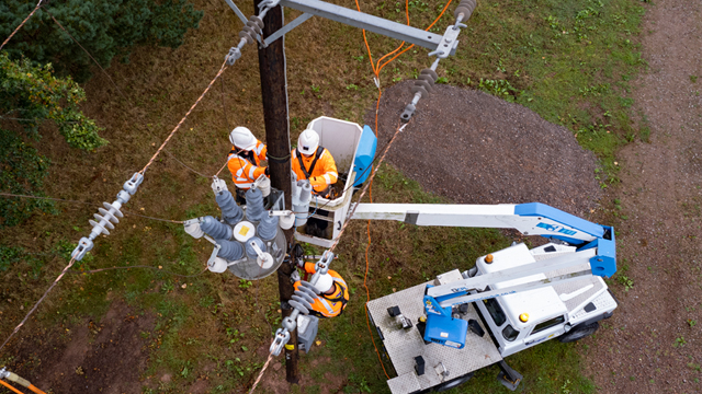 Three engineers wearing full PPE working on overhead electricity lines, two climbing the pole and one in a cherry picker basket