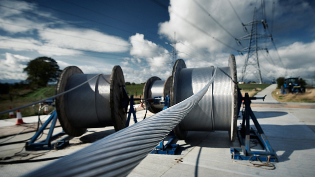 Large spools of overhead electricity lines with electricity pylon in the background