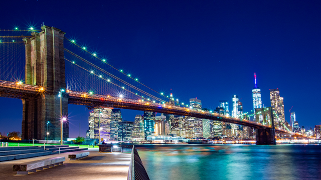 New York Brooklyn Bridge at night with Manhattan lit up in the background against a vivid blue sky