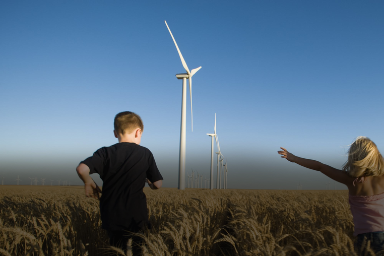 children in a field with wind turbines