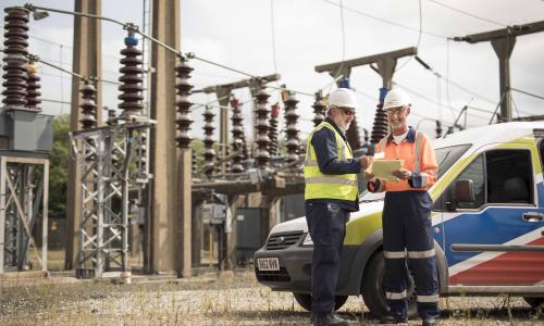 Two National Grid employees standing in front of an electricity plant and a National Grid vehicle 