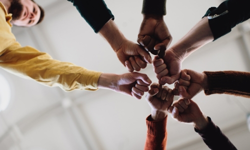 People standing in a circle holding their fists in seen from underneath