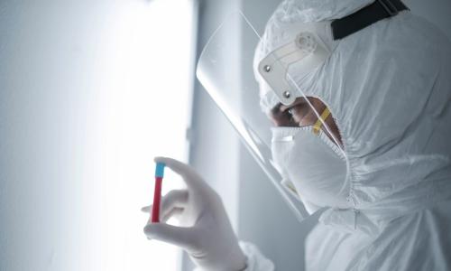 Person wearing full PPE holding blood vial used for National Grid 'Backing the quest for a COVID-19 vaccine' story