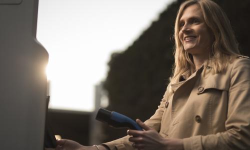 Woman wearing a trench coat about to put an EV charger into a charging point