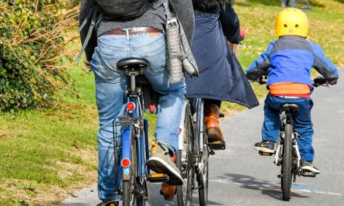 Two adults and a child wearing a yellow helmet cycling on path