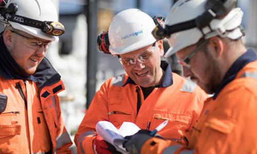 Three National Grid construction engineers wearing hard hats and PPE discussing paperwork