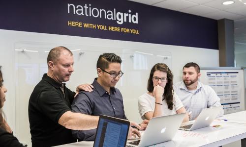 Five National Grid representatives working at a high desk with a white board in the background 
