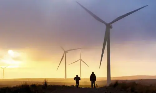 Two people standing under a wind turbine at sunset for National Grid article