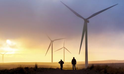 Two people standing under a wind turbine at sunset for National Grid article