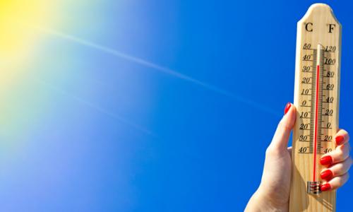 Hand holding thermometer showing high temperatures in the sun